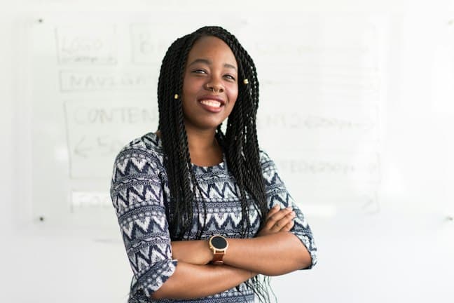 Une collaboratrice souriante, bras croisés, devant un tableau blanc couvert de notes